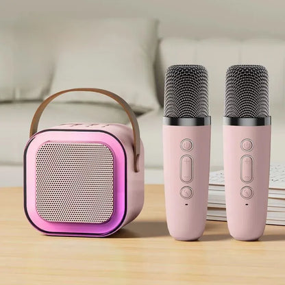 Pink portable speaker and two microphones on a wooden surface with a blurred background
